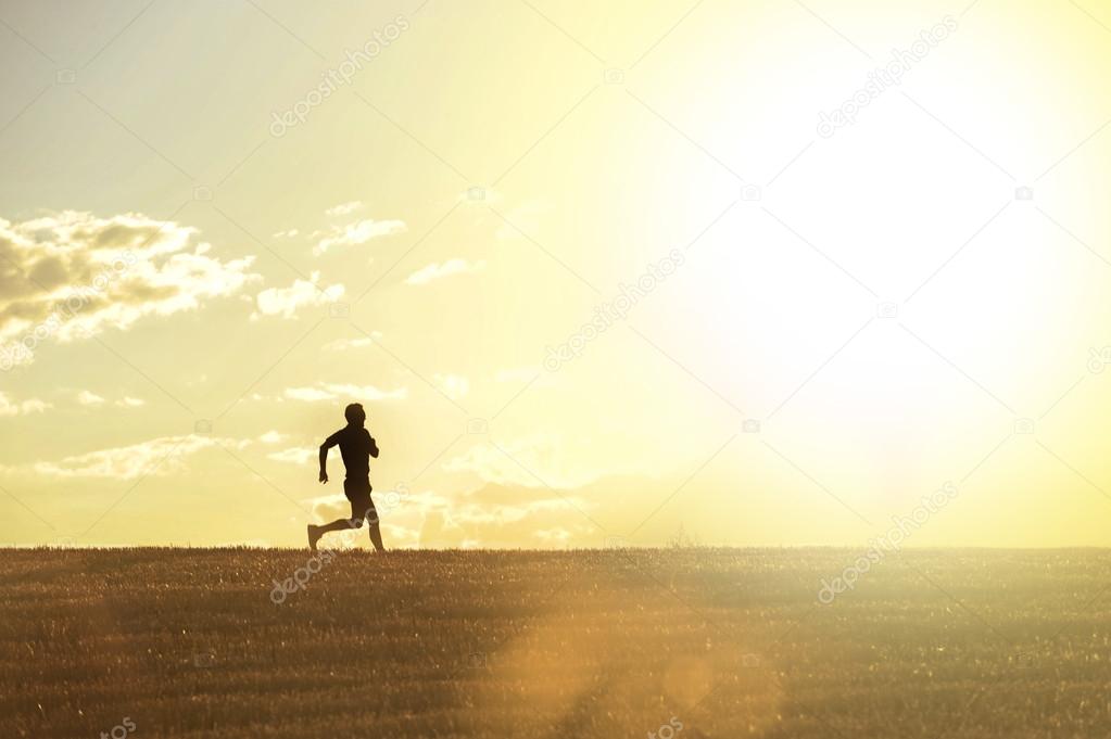 Profile silhouette of young man running in countryside training cross country jogging discipline in summer sunset on beautiful rural landscape