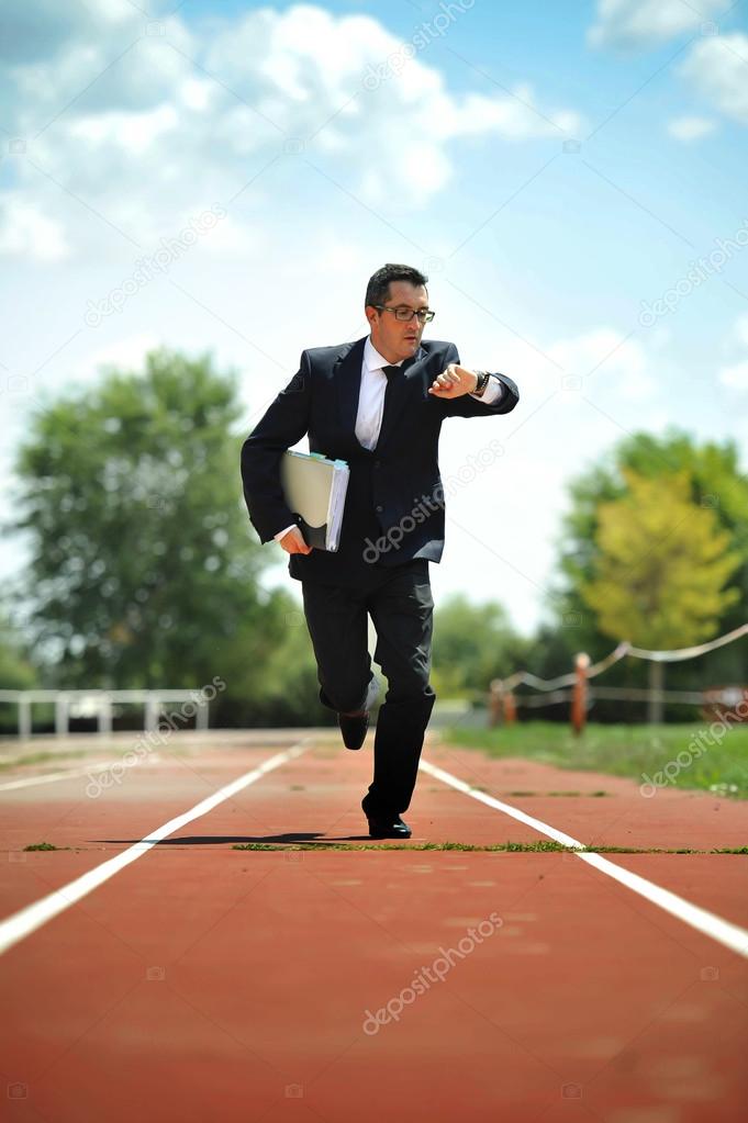 businessman looking wrist watch watch running on athletic track in stress