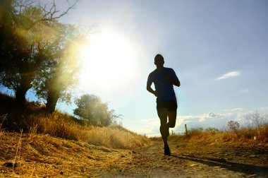 front silhouette young sport man running cross country workout at summer sunset