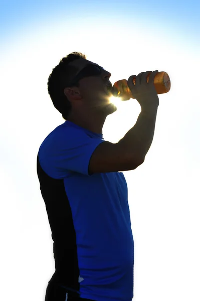 Dunkle Silhouette eines jungen gesunden Sportlers, der nach einer Trainingseinheit isotonisches Getränk trinkt — Stockfoto