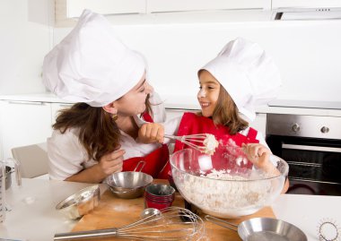 happy mother baking with little daughter in apron and cook hat with flour dough at kitchen