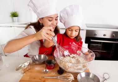 happy mother baking with little daughter in apron and cook hat with flour dough at kitchen