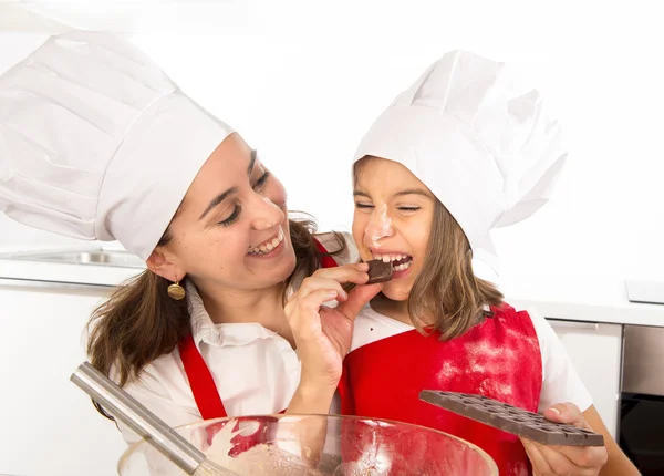 Happy mother baking with little daughter eating chocolate bar used as ingredient while teaching the kid — Stock Photo, Image