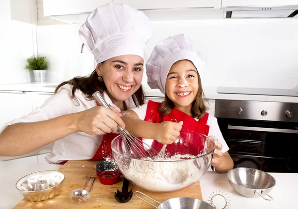 Happy mother baking with little daughter in apron and cook hat with flour dough at kitchen — Stock Photo, Image