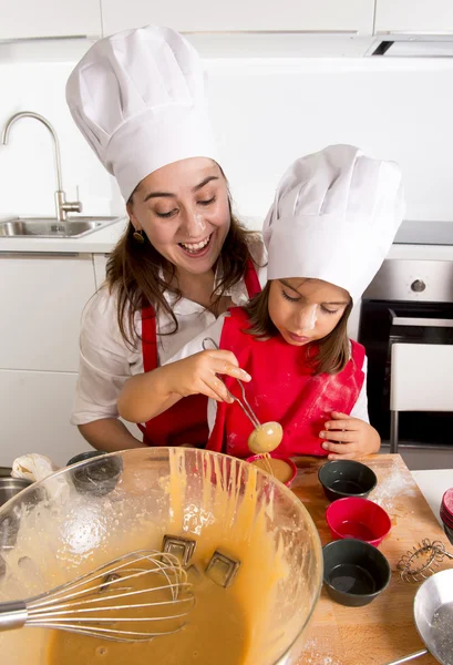 Mother baking with little daughter in apron and cook hat filling mold muffins with chocolate dough — Stock Photo, Image