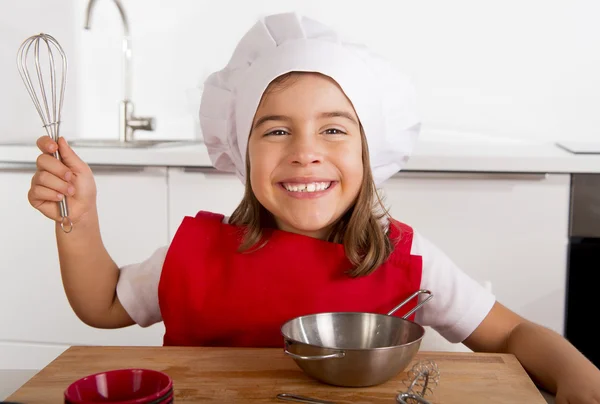 Sweet little girl in red apron and cook hat playing chef learning cooking at home kitchen — Stock Photo, Image