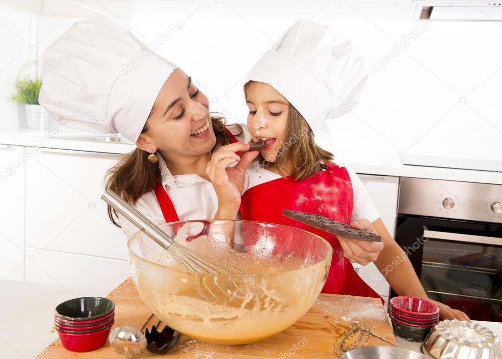 happy mother baking with little daughter eating chocolate bar used as ingredient while teaching the kid