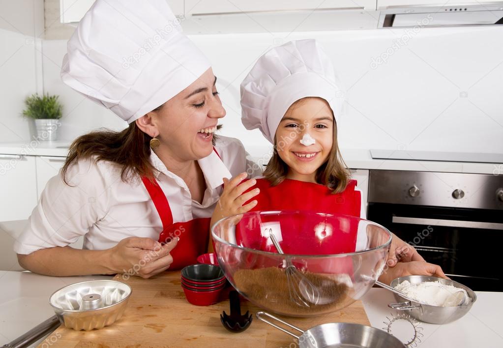 happy mother baking with little daughter in apron and cook hat with flour dough at kitchen