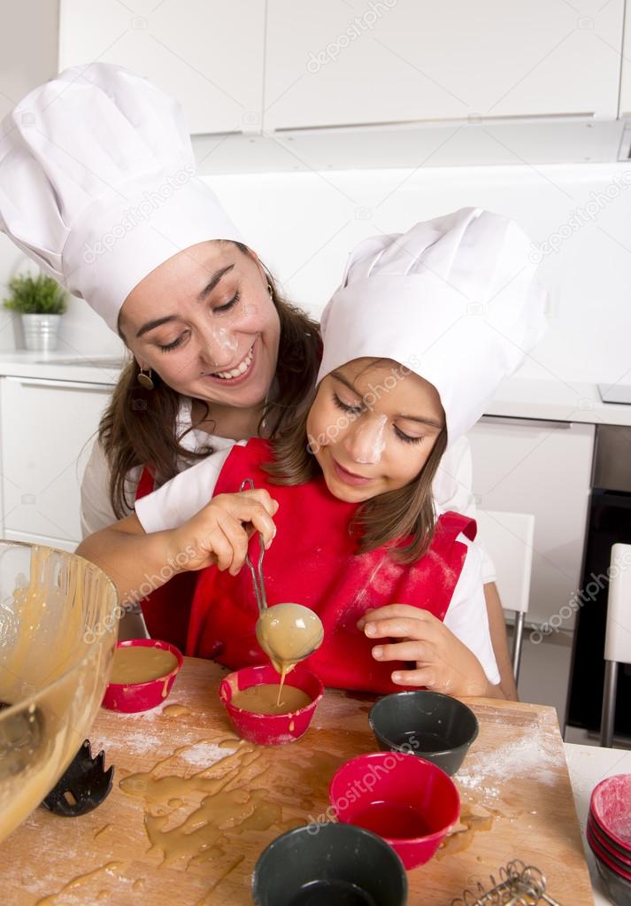 mother baking with little daughter in apron and cook hat filling mold muffins with chocolate dough