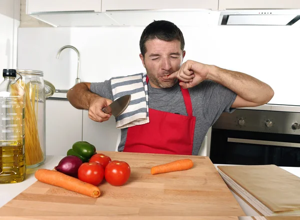 Home cook man in rode schort wortel met keukenmes lijden binnenlandse ongeval snijden kwetsen vinger snijden — Stockfoto