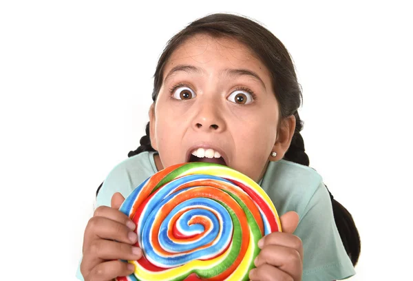 Feliz niña sosteniendo gran caramelo piruleta mordiendo el caramelo con sus dientes en loca expresión de cara divertida — Foto de Stock