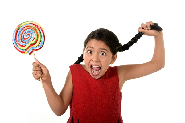Happy female child holding big lollipop candy pulling pony tail with crazy funny face expression in sugar addiction — Stock fotografie