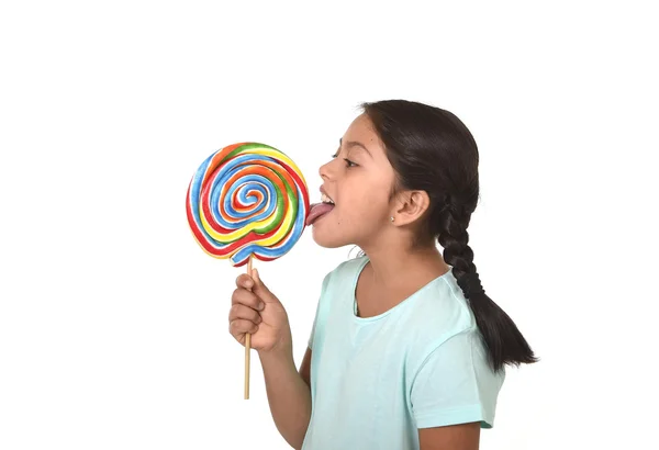 Happy female child holding big lollipop candy licking the candy with her tongue in sugar addiction — Zdjęcie stockowe