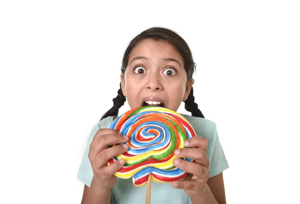 Feliz niña sosteniendo gran caramelo piruleta mordiendo el caramelo con sus dientes en loca expresión de cara divertida — Foto de Stock