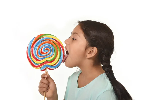 Happy female child holding big lollipop candy licking the candy with her tongue in sugar addiction — Stockfoto