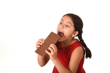 Hispanic female girl wearing red dress holding with both hands big chocolate eating in happy excited face expression in sugary nutrition