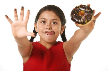 latin female child in red dress holding chocolate donut with hands and mouth stained and dirty showing tongue happy