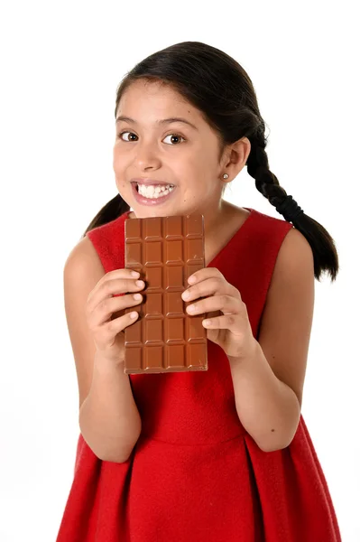 Ragazza ispanica donna che indossa abito rosso tenendo con entrambe le mani grande cioccolato mangiare in felice espressione viso eccitato in nutrizione zuccherina — Foto Stock