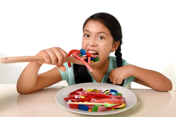 Happy young girl holding spoon eating from dish full of candy lollipop and sugary things — Stok fotoğraf