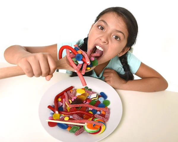 Happy young girl holding spoon eating from dish full of candy lollipop and sugary things — Stok fotoğraf