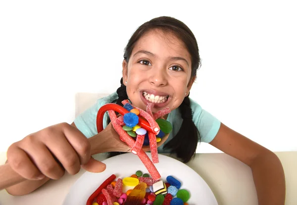 Happy young girl holding spoon eating from dish full of candy lollipop and sugary things — 图库照片