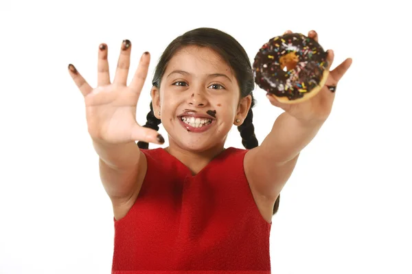 Латинська молода дівчина в червоній сукні тримає шоколадний пончик руками і ротом заплямована і брудна, показуючи усміхнений щасливий — стокове фото