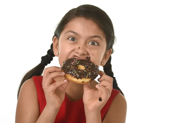 Іспано-жіноча дитина в червоній сукні їсть шоколадний пончик з руками і ротом заплямований і брудний усміхнений щасливий — стокове фото