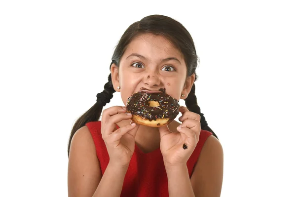 Hispanik anak perempuan dalam gaun merah makan donat cokelat dengan tangan dan mulut kotor tersenyum bahagia — Stok Foto