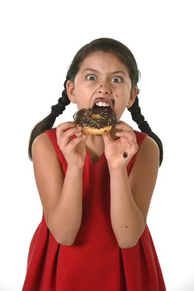 Niña hispana vestida de rojo comiendo rosquilla de chocolate con las manos y la boca manchada y sucia sonriente feliz —  Fotos de Stock