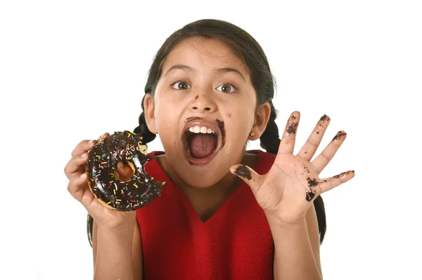 Hispanic female child in red dress eating chocolate donut with hands and mouth stained and dirty smiling happy — Zdjęcie stockowe