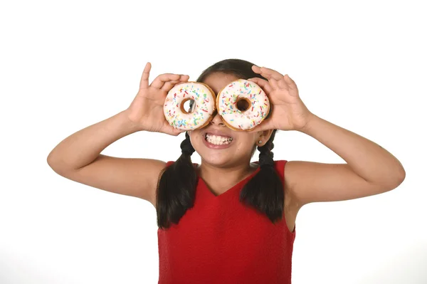 Latin child in red dress playing with donuts in her hands putting them on her face as cake eyes — Zdjęcie stockowe