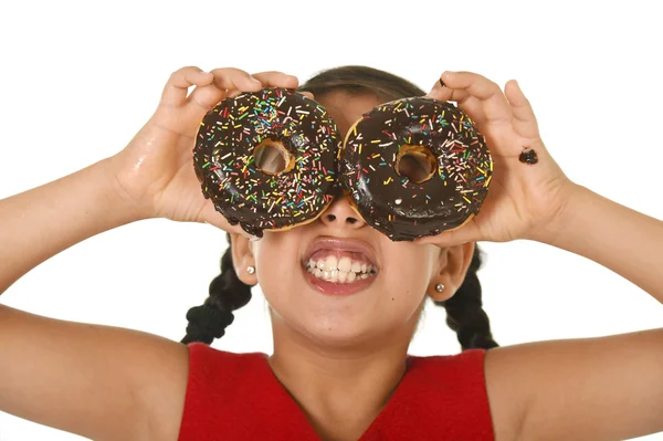 Lateinisches Kind im roten Kleid, das mit Donuts in ihren Händen spielt und sie als Kuchenaugen auf ihr Gesicht legt — Stockfoto