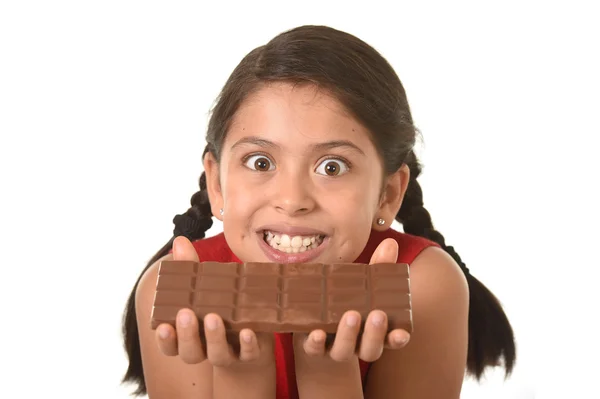 Latin child in red dress holding with both hands big chocolate bar in front of her crazy excited face expression — Stock Photo, Image