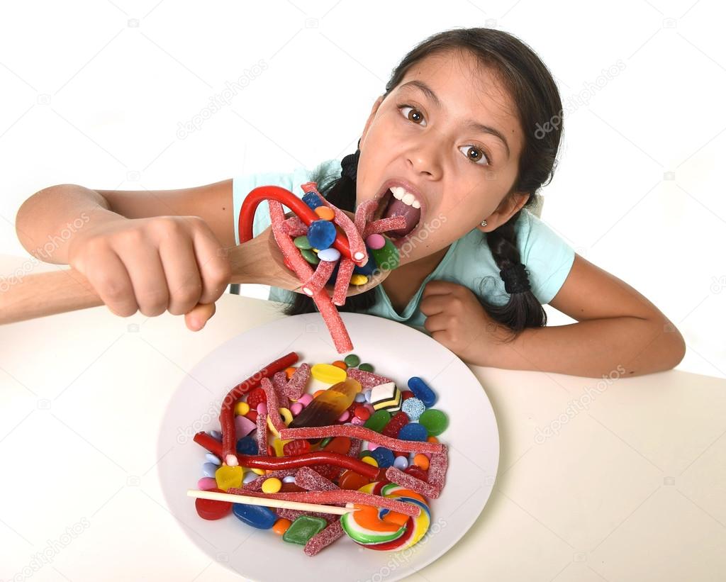 happy young girl holding spoon eating from dish full of candy lollipop and sugary things