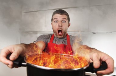 inexperienced home cook with apron holding pot burning in flames