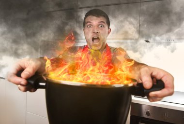 inexperienced home cook with apron holding pot burning in flames