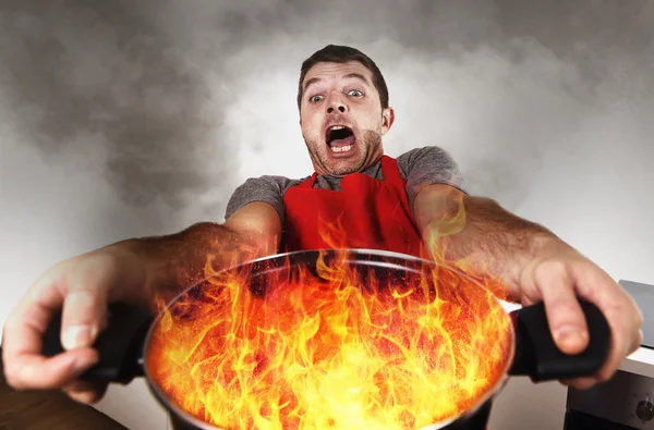 Inexperienced home cook with apron holding pot burning in flames — Stock Photo, Image