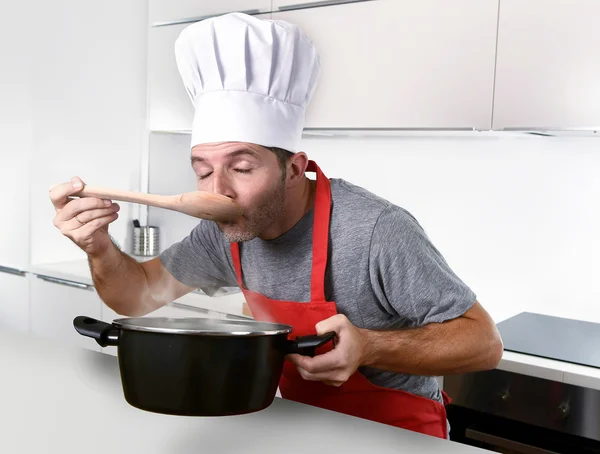 Joven atractivo hombre en sombrero de chef y delantal rojo cocinero prueba flav — Foto de Stock