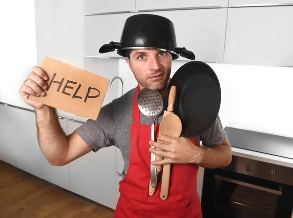 Funny man holding pan with pot on head in apron at kitchen askin — Stockfoto