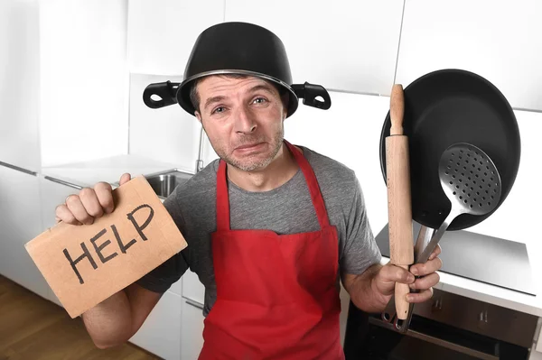 Funny man holding pan with pot on head in apron at kitchen askin — Zdjęcie stockowe