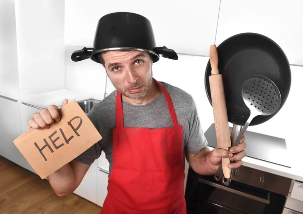 Funny man holding pan with pot on head in apron at kitchen askin — Stockfoto