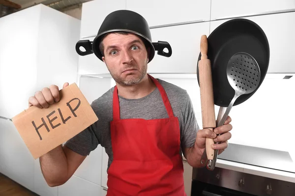 Funny man holding pan with pot on head in apron at kitchen askin — Stok fotoğraf