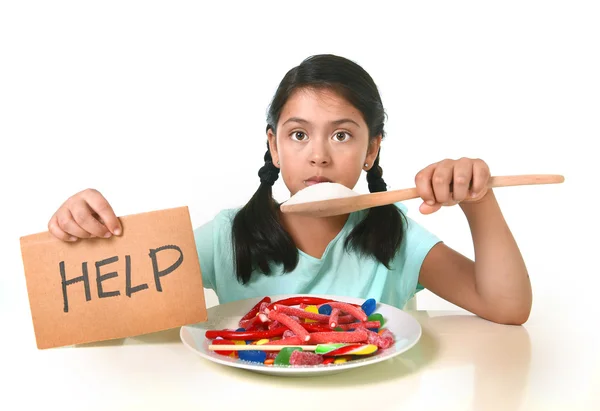 Bambino che mangia zucchero dolce in un piatto di caramelle con un cucchiaio di zucchero che chiede aiuto in un concetto nutrizionale malsano — Foto Stock