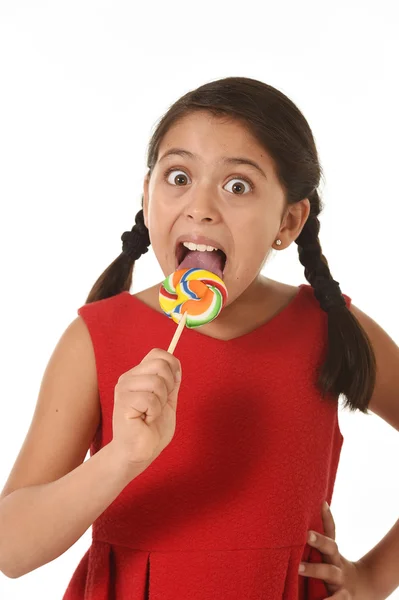 Dolce bella latina femmina bambino tenendo caramelle lecca lecca mangiare e leccare felice ed eccitato — Foto Stock