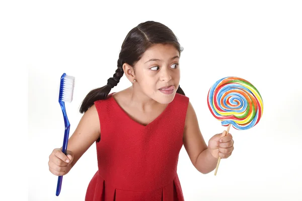 Lindo niño femenino sosteniendo gran espiral caramelo piruleta y enorme cepillo de dientes en el cuidado dental y el concepto de salud —  Fotos de Stock