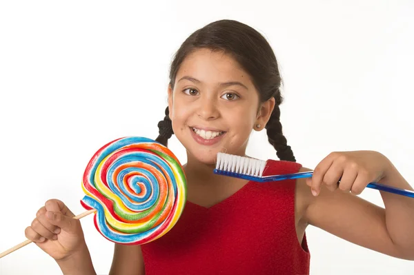 Cute female child holding big spiral lollipop candy and huge toothbrush in dental care and health concept — ストック写真