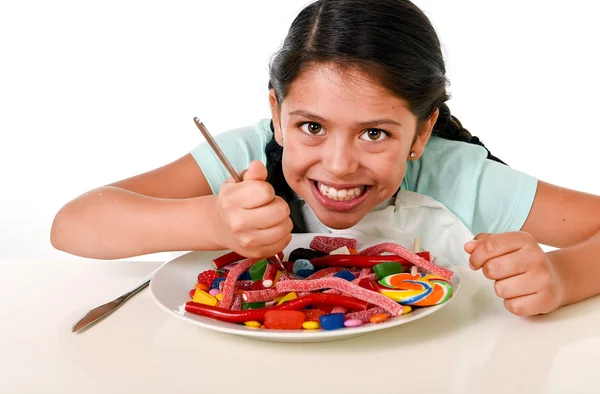 Anak perempuan Latin yang bahagia makan hidangan penuh permen dan permen karet dengan garpu dan pisau dan botol cola besar dalam penyalahgunaan gula — Stok Foto