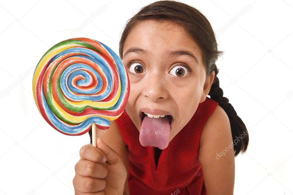 sugar addict latin female child holding huge lollipop candy eating and licking happy crazy excited