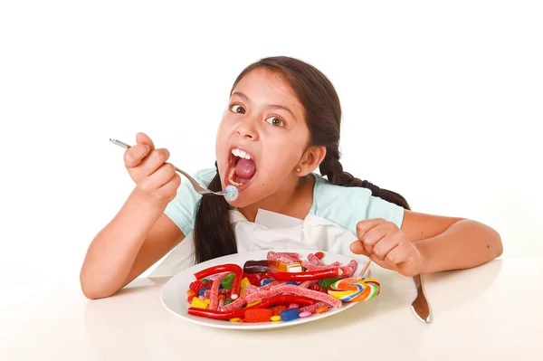 Happy Latin female child eating dish full of candy and gummies w — Stock Photo, Image