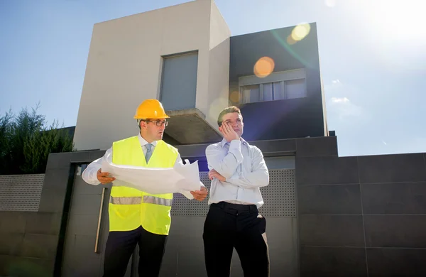 Client malheureux dans le stress et constructeur contremaître travailleur avec casque et gilet argumenter à l'extérieur sur les plans de construction de maisons neuves — Photo